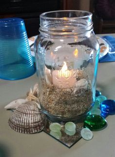 a glass jar filled with sand and sea shells sitting on top of a white table