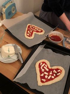 two uncooked heart shaped pizzas sitting on top of baking pans next to each other