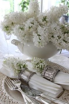 a white table setting with flowers in a vase and silverware on the placemats