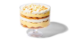 a layered cake with whipped cream and oranges on top sits in a glass dish