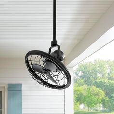 an outdoor fan is hanging from the ceiling in front of a white house with blue shutters