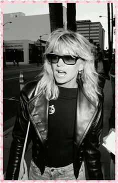 a black and white photo of a woman walking down the street with sunglasses on her face