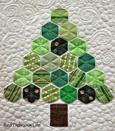 a quilted christmas tree made with green and black hexagons on white fabric