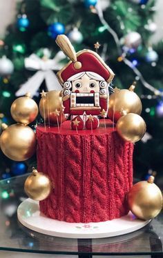 a christmas cake decorated with gold ornaments and a santa clause head on top, sitting in front of a christmas tree