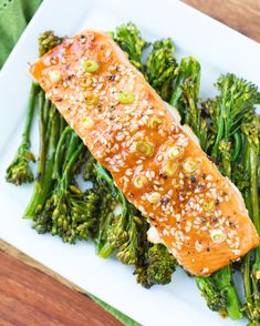 a piece of salmon with sesame seeds and broccoli on a white square plate