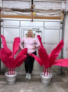 a woman standing next to two large pink flowers in buckets on top of a floor