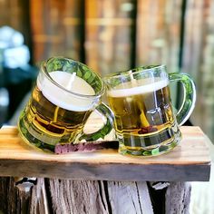 two mugs of beer sitting on top of a wooden table next to each other