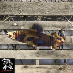 a metal fish sitting on top of a wooden fence