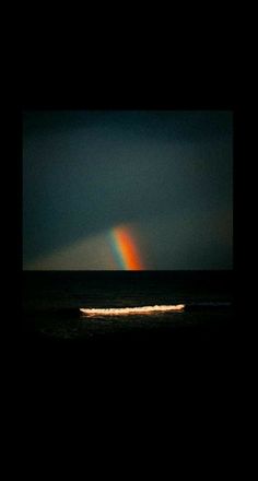 a rainbow appears over the ocean with a boat in the foreground