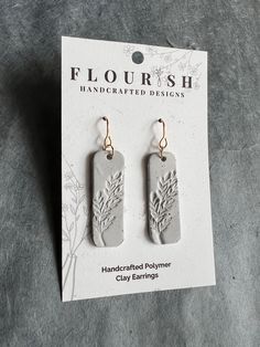 two small tags with flowers on them are sitting in front of a card that says, floursh handcrafted polymer clay earrings