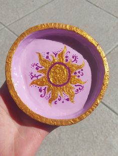 a hand holding a small purple and gold bowl with a sun design on the side