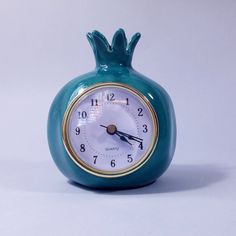 a small blue ceramic clock with a gold trim around the face on a white background