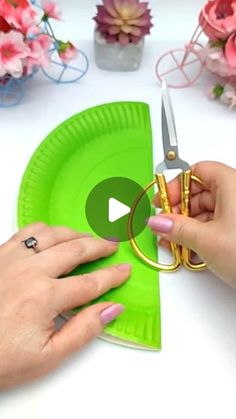 two hands holding scissors over a green paper plate on a table with flowers in the background