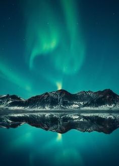 the aurora bore is reflected in water with mountains and snow capped peaks behind it, as well as green lights