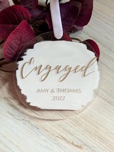 a glass ornament with the word engaged on it next to some purple flowers