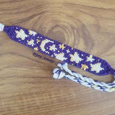 a purple and white beaded lanyard sitting on top of a wooden table