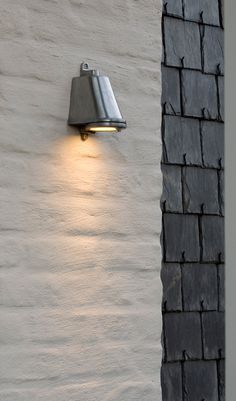 a wall light mounted on the side of a white brick building with black shingles