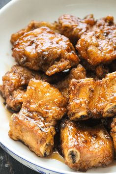 a white bowl filled with chicken wings covered in sauce on top of a wooden table