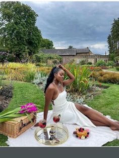 a woman sitting on top of a white towel next to a table filled with fruit