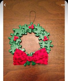 a christmas wreath ornament made out of puzzle pieces on a wooden table with a red bow