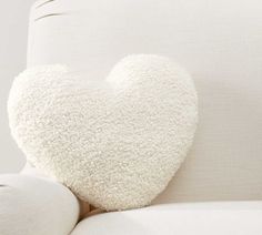 a white heart shaped pillow sitting on top of a couch next to a leg rest