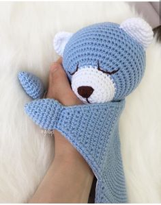 a crocheted blue teddy bear is held by someone's hand