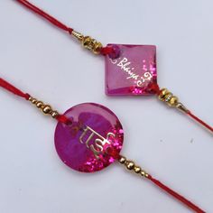 two necklaces with pink and gold designs on red string, one has an ombrella