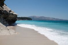 a sandy beach next to the ocean under a blue sky with mountains in the background