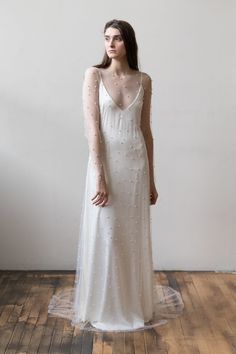 a woman in a long white dress standing on a wooden floor with her back to the camera