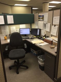 an office cubicle with two computer screens and several papers on the desk