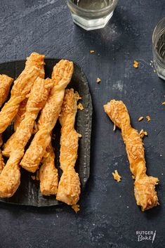 some fried food on a black plate next to two cups and spoons with water