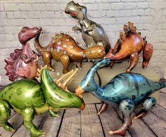 several inflatable dinosaurs are lined up against a brick wall on a wooden floor