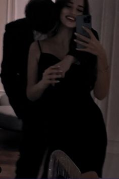 a woman taking a selfie with her cell phone in front of the camera, wearing a black dress