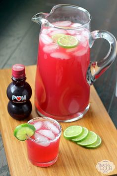 a pitcher of red liquid next to a glass with limes on it and a bottle of soda