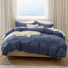 a bed with blue comforter and pillows in front of a window overlooking the ocean