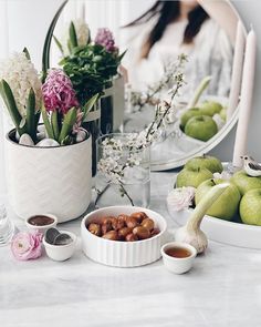 a table topped with bowls filled with fruit and flowers next to a mirror on top of a counter