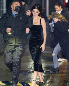 a man and woman walking in the rain under an umbrella while wearing face coverings