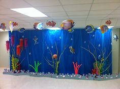 an office cubicle is decorated with fish and corals on the walls, along with blue curtains