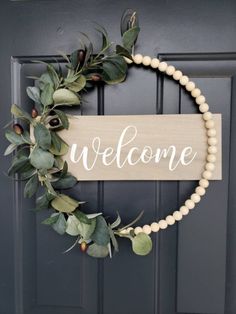 a welcome sign hanging on the front door with greenery and beads around it's edges