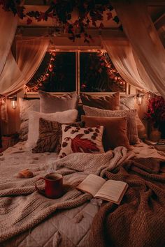 a bed with blankets, pillows and coffee cup on it in front of a window