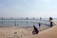 people are standing on the beach and in the water near a pier with a boat