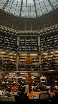 people sitting at tables in a library with many books on the shelves and skylight overhead