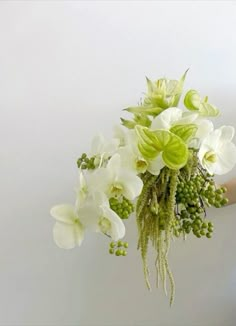 a woman holding a bouquet of white flowers in her right hand and green berries on the left