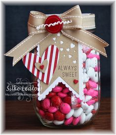 a jar filled with lots of candy sitting on top of a wooden table next to a brown ribbon