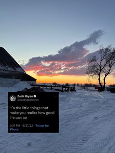 a sign that is in the snow near a tree and building with a sunset behind it