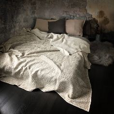 an unmade bed sitting on top of a wooden floor next to a brick wall