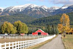 a red barn sits on the side of a dirt road in front of snowy mountains