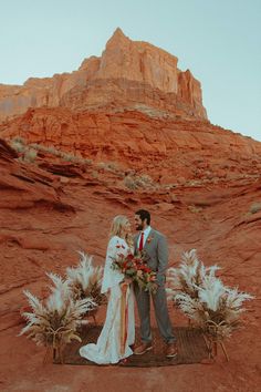 a bride and groom standing in front of red rocks at their desert wedding ceremony with flowers