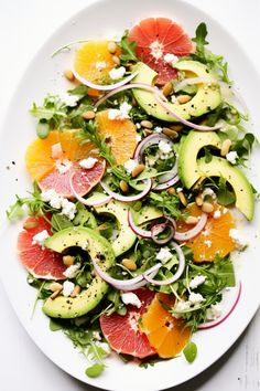 a white plate topped with sliced oranges, avocado and spinach salad