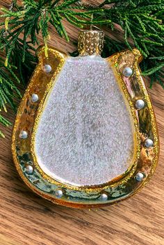 an ornament hanging from a christmas tree on a wooden table with pine needles